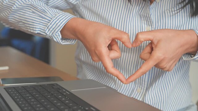 Business Professional Making Heart Gesture above Laptop in Modern Workplace. Concept Customer Care, Appreciation, Trust, Teamwork, Partnership, Positive cCommunication, Strong Business Relationships