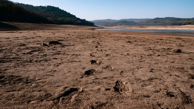 Footprints mark the dusty earth around a scorched empty reservoir conveying a sense of enduring harmony