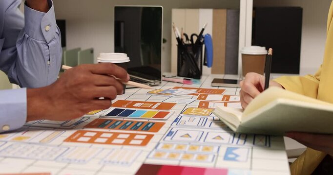 Creative team collaborating on UX and UI design using wireframes, interface components, color palettes, and planning materials to develop digital products through design thinking and teamwork.