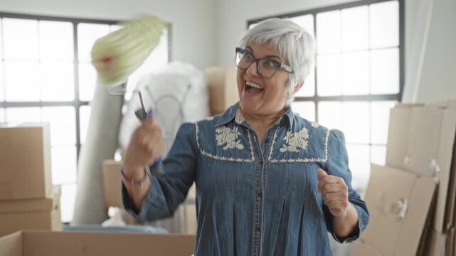 Woman laughing and holding paint roller with outstretched hand among moving boxes in building; home renovation joy.