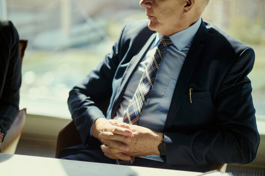 Close up of senior Caucasian businessman sitting with folded hands during boardroom meeting, discussing strategy and leadership. Useful for energy sector management or executive planning