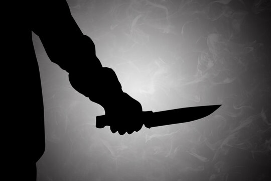 Mysterious dark silhouette of a hand holding a knife, presented against a moody, smoky background
