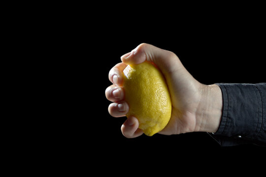 Male hand squeezing a lemon tightly on black background for business pressure concept with copyspace