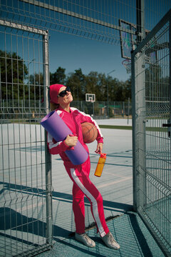 Confident active 60 years old senior woman in pink tracksuit holding sports equipment on outdoor court