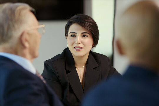 Close up of young adult businesswoman leading discussion with senior male colleagues during oil industry meeting, supporting corporate leadership, energy strategy marketing