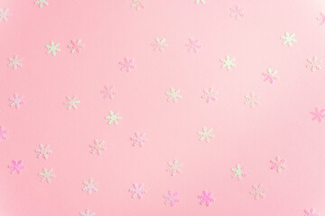 Pink background with iridescent snowflake confetti scattered in a festive winter pattern with soft...