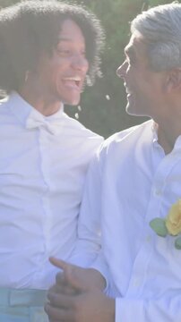 Vertical video: Laughing grooms in white shirts holding hands at wedding, guests blowing bubbles