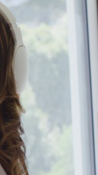 Vertical video: Listening woman smiling, gesturing to music starting by window with headset, shirt