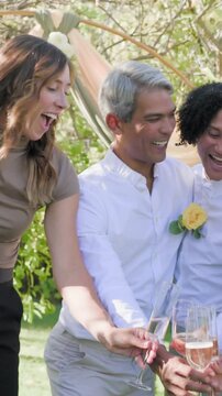 Vertical video: Reacting to offscreen cue, friends clinking flutes in garden, yellow rose