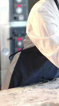 Vertical video: Leaning white-coated chef in jean apron stretching dough for baking, copy space