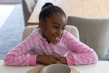 African American child girl smiling at home table in pink fleece, with bowl, placemat, chopsticks © wavebreak3