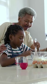 Vertical video: Placing hand showing whisk, grandma guiding girl in apron at kitchen mixing batter