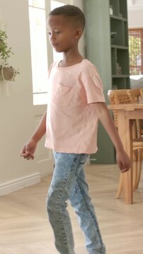 Vertical video: Child walking in pink tee climbing onto green-shirt dad at home, looking at phone