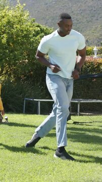 Vertical video: Tapping father keeping soccer ball in yard, guiding child yellow-top approaching