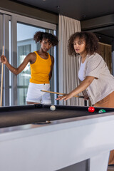 Naklejka premium Diverse females playing pool at table with wooden cues in rec room, one lining up shot