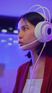 Excited young Asian girl playing online computer game with headset and microphone at home, esports and live streaming concept