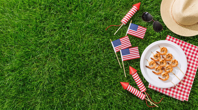 4th of July Independence Day seafood picnic background with grilled shrimp skewers, American flags, fireworks rockets, picnic blanket, straw hat and green grass copy space for patriotic celebration