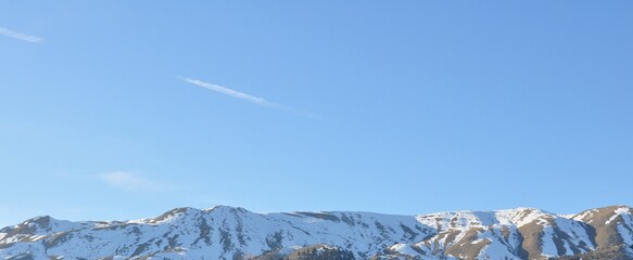 Snowy peak of mountain and Minimalist sky background featuring a bright blue atmosphere and a thin aircraft contrail crossing the frame. ideal for  travel, freedom, weather, and background concepts. © Olga