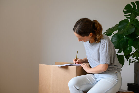Woman writing moving house checklist standing by boxes