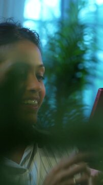 Indian businesswoman checking mobile phone at desk in modern cozy office, Asian female glued to smartphone while multitasking during office hours, smiling with positive body language in workplace