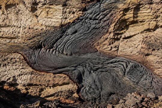 Cross-section of cooled volcanic lava flow fused with bedrock, contrasting textures.