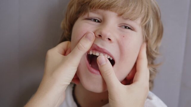 Mother checks her six-year-old son's loose upper primary incisor and supernumerary tooth, supporting his changing teeth journey with a cheerful cheek pinch