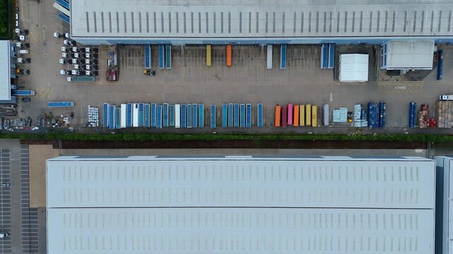 Aerial view of commercial warehouses with loading bays, parked trucks, and trailers at a logistics facility in Kettering, England, United Kingdom.
