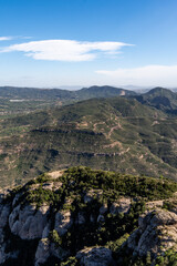Fototapeta premium Breathtaking aerial vista of the lush green mountain terrain and valleys in the Montserrat region of Catalonia, Spain, under a clear, bright sky with light wispy clouds.