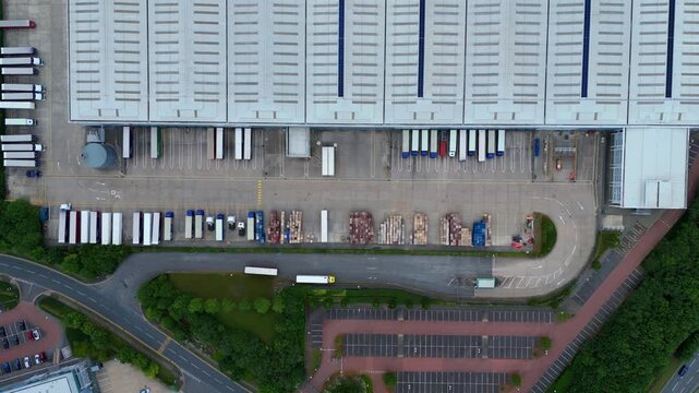 Aerial view of commercial warehouses with loading docks and parked semi-truck trailers at a logistics facility in Kettering, England, United Kingdom.