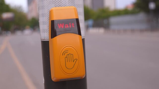 Close up view of a person's hand pressing a yellow pedestrian crossing button, activating the signal to cross the street safely while waiting for traffic to stop at the city intersection