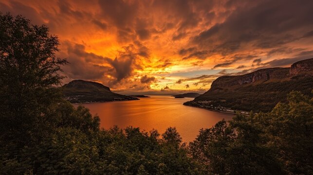 Orange and yellow sunset over a calm bay with silhouetted hills and trees