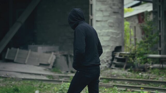 Suspicious middle-aged man in hoodie walking through abandoned metal factory