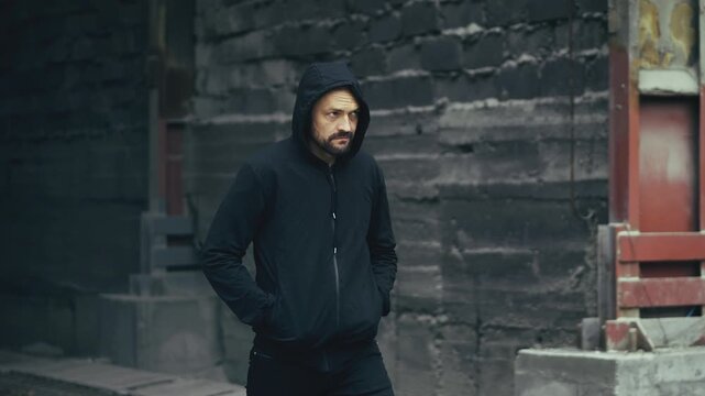 Middle-aged man in hoodie walking through industrial area, suspicious activity
