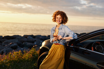 Fototapeta premium Cheerful woman outdoors by a car, smiling in a denim jacket and yellow skirt, sunset light, coastal breeze, candid lifestyle moment, bright natural colors and relaxed posture