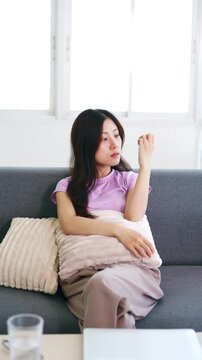 ASian girl sitting on home couch, looking away, thinking on nothing, troubles, looking away with apathy, feeling loneliness, fatigue, depression