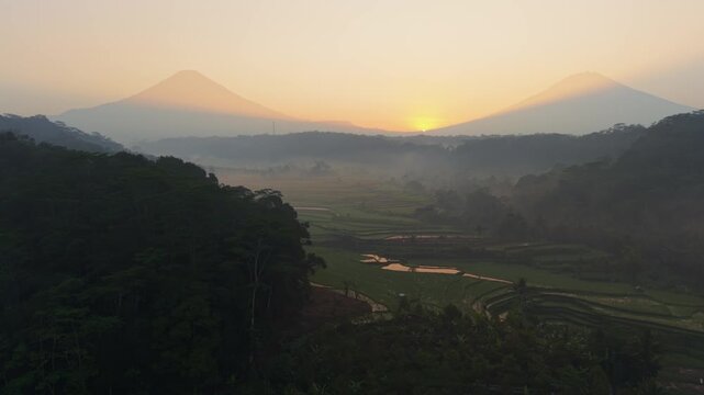 Aerial view of the misty volcanic landscape at sunrise with lush rice terraces in Selomerto, Central Java, Indonesia.
