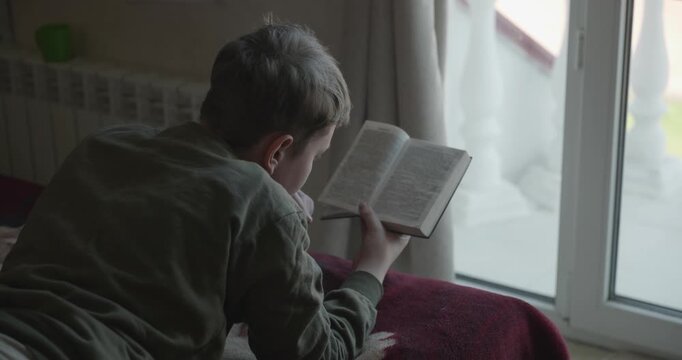 Caucasian Boy Kid Read Bible Book Lying on Bed in Bedroom. 4K 10-bit