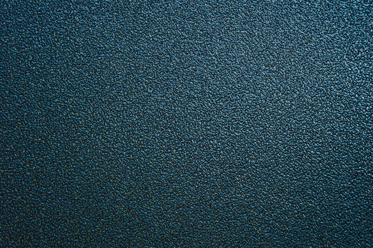 Close-up of a dark blue teal grainy textured surface. Abstract background with fine rough details, metallic glitter effect.