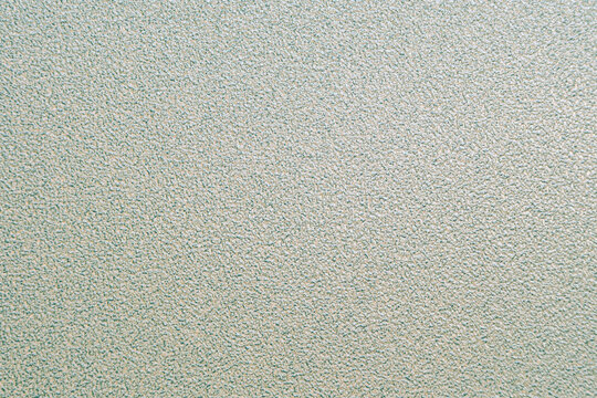 Close-up of a light sage green gray grainy textured surface. Abstract neutral background with fine rough details, plaster or stucco effect.