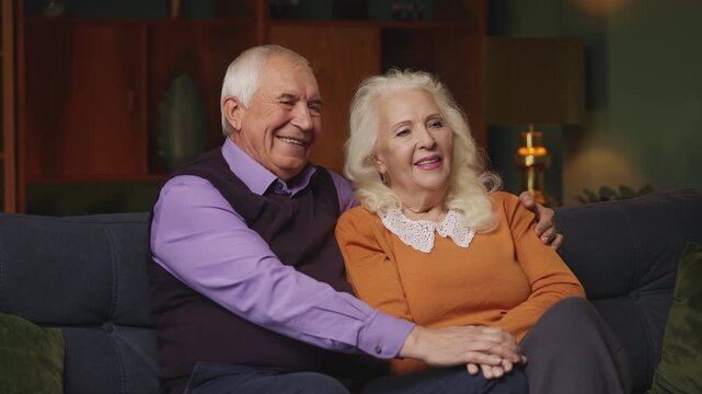 Cheerful senior couple sitting on sofa and hugging, warm loving relationship