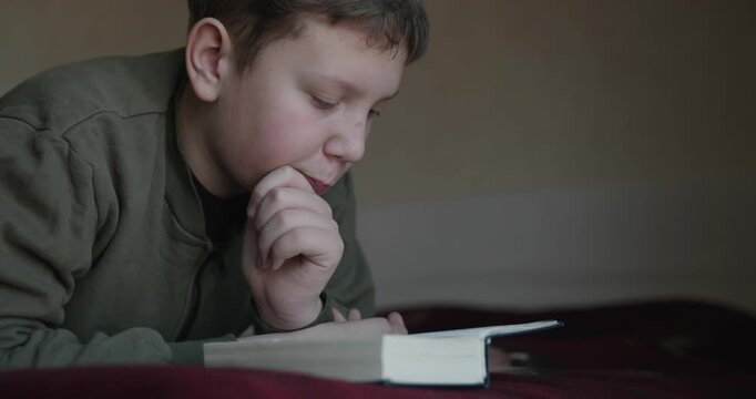 Caucasian Boy Kid Read Bible Book Lying on Bed in Bedroom. 4K 10-bit