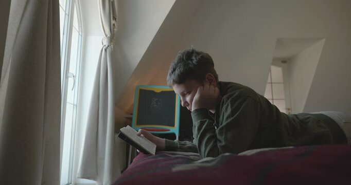 Caucasian Boy Kid Read Bible Book Lying on Bed in Bedroom. 4K 10-bit