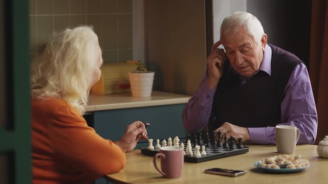 Happy elderly couple enjoying a chess game at home, spending time together
