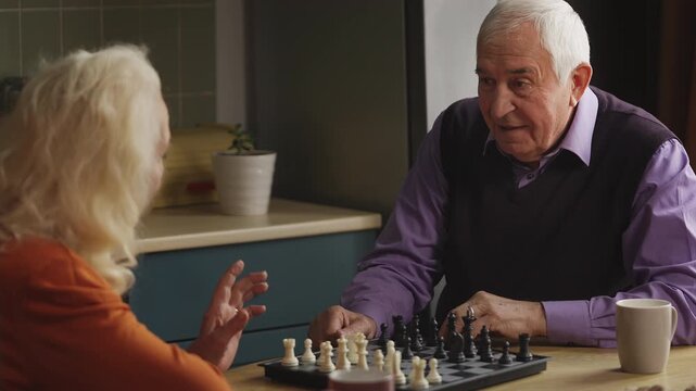 Couple in their 70s playing chess in the kitchen, celebrating with a high five