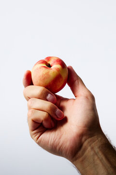 Hand holding a fresh ripe peach against white background