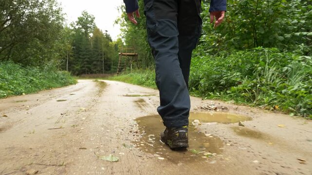 Camera following muddy boots pacing through puddles on a dirt road