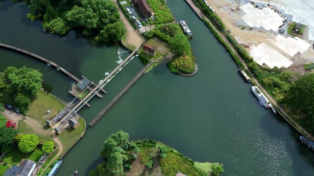 Aerial view of Feildes Weir Lock with narrowboats moored along the river banks and lush green surroundings in Hoddesdon, England, United Kingdom.