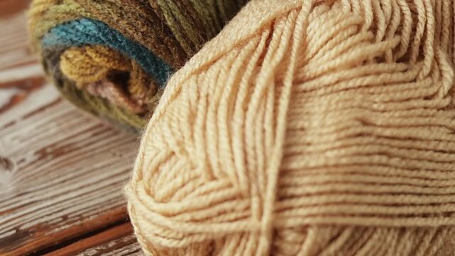 Slow macro pan across beige and multicolor yarn skeins on rustic wood. Detailed wool texture for crafting, knitting, and cozy lifestyle backgrounds.