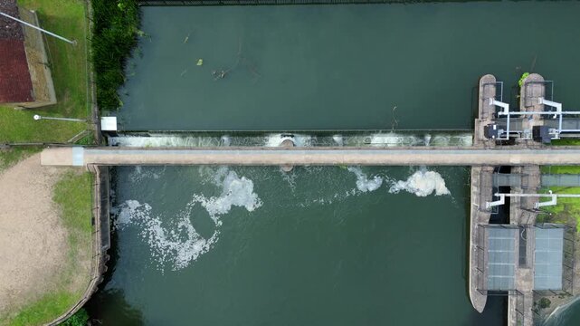 Aerial view of Feildes Weir Lock with water flowing over the weir and white foam in the river at Hoddesdon, England, United Kingdom.