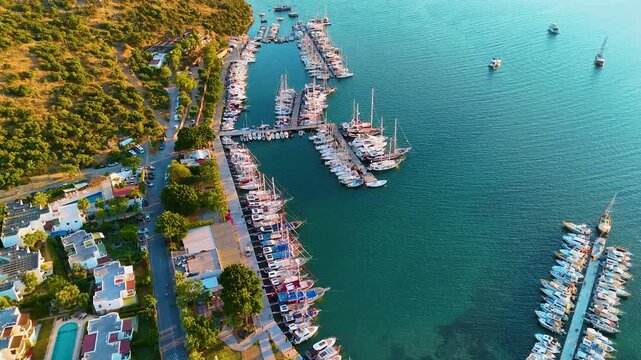 Cinematic aerial drone slow forward shot over Bitez Marina with sailing yachts, Turkish gulet boats and luxury motorboats at golden hour sunset, Bodrum Aegean coast Mugla Turkey